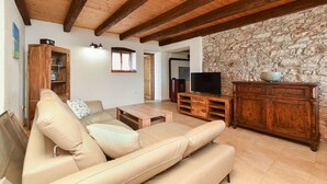 A living room with a beige sofa, wooden entertainment unit, stone wall, and exposed wooden beams.