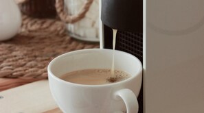 Eine weiße Tasse wird aus einem schwarzen Behälter mit einem Getränk, vermutlich Kaffee, gefüllt.
