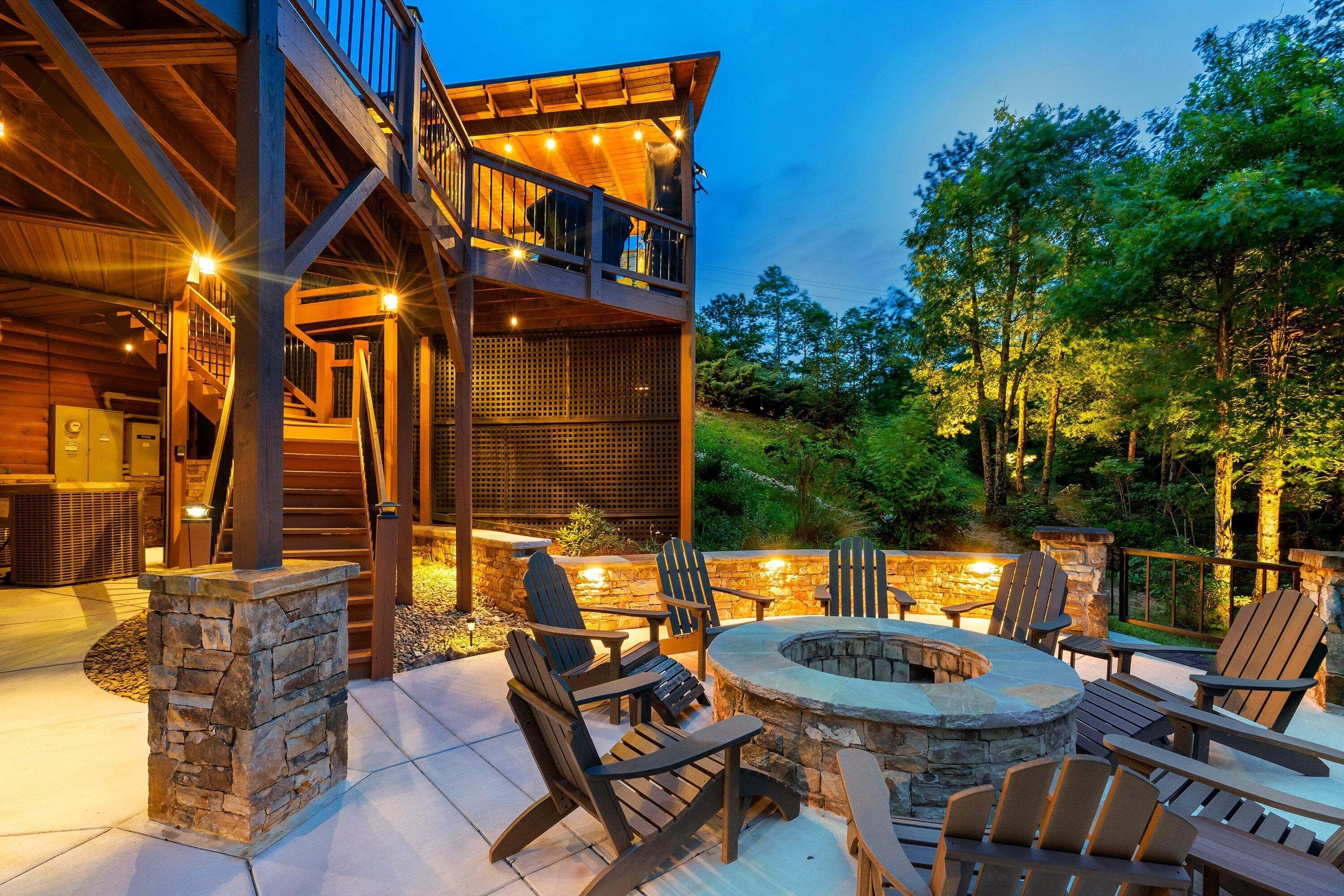 A two-story wooden cabin with a deck, outdoor seating area, and a stone fire pit.
