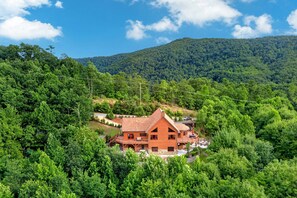 Une cabane en bois dotée d’un balcon, entourée d’une forêt dense et de collines.