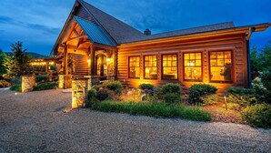 Eine Holzblockhütte mit Veranda, Steinpfeilern und einer Schotterzufahrt.