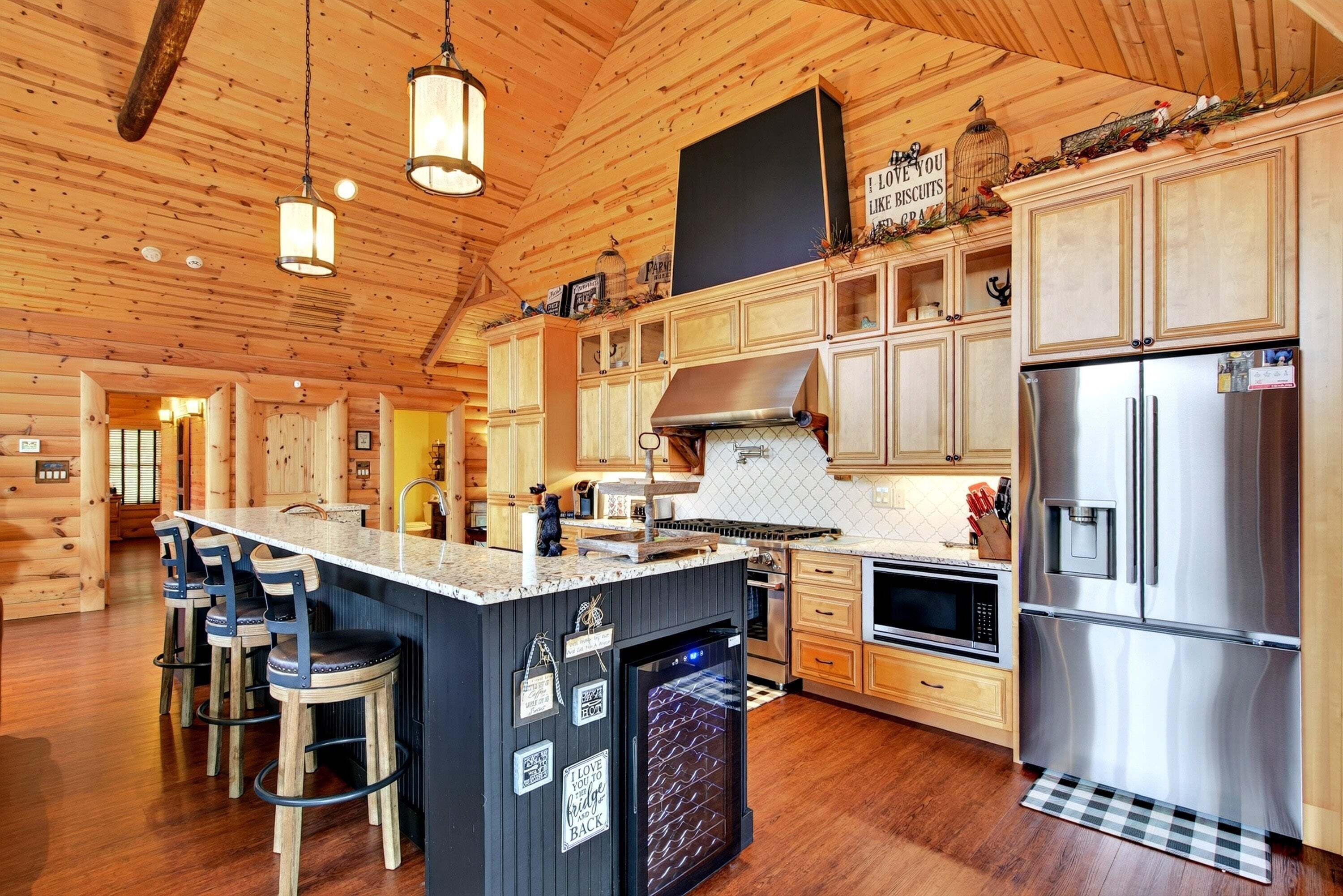 A spacious kitchen with wooden cabinets, a central island with bar stools, stainless steel appliances, and a hanging light fixture.