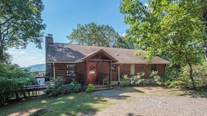 A rustic log cabin with a red door, a porch, and a gravel driveway.