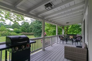 Eine überdachte Veranda mit Grill, Gartenmöbeln und Blick auf einen üppigen Garten.