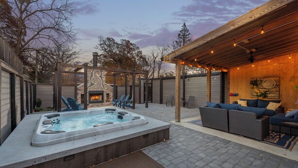 Een achtertuin met een hottub, buitenzitplaatsen en een overdekt gebied met lichtslingers.