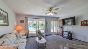 A living room with a sofa, a coffee table with flowers, a ceiling fan, a TV, and a door leading outside. - Comfy Country home. Pet friendly, 5 bedrooms, AC, WIFI, just outside Farmington  (Farmington)