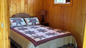 Un dormitorio con paneles de madera, una cama, una ventana y una mesita de noche.