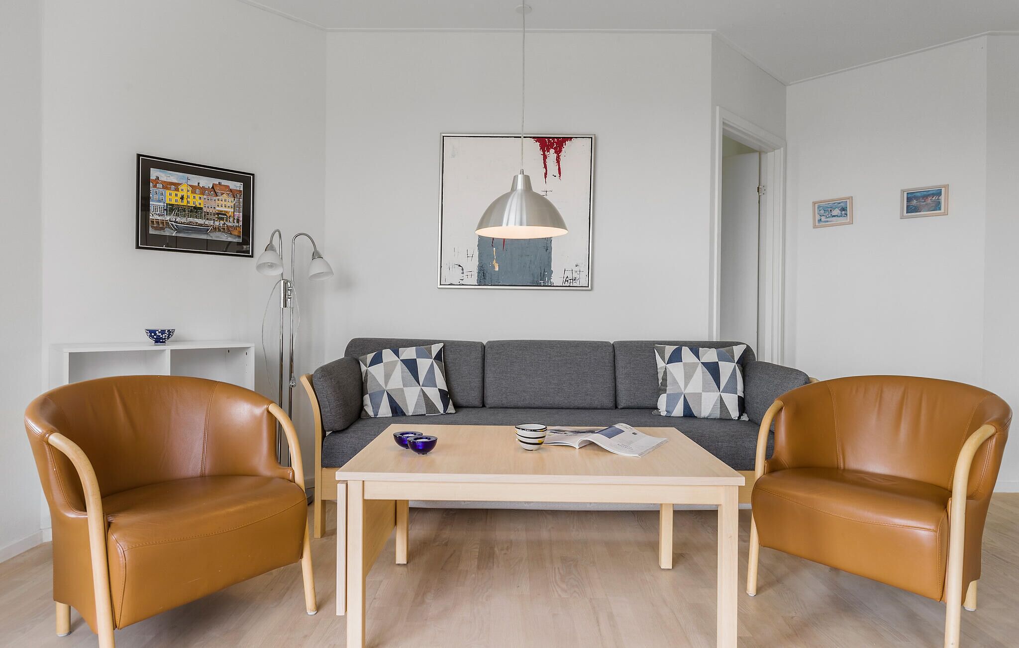 A modern living room with a grey sofa, two leather armchairs, a wooden coffee table, and a floor lamp.