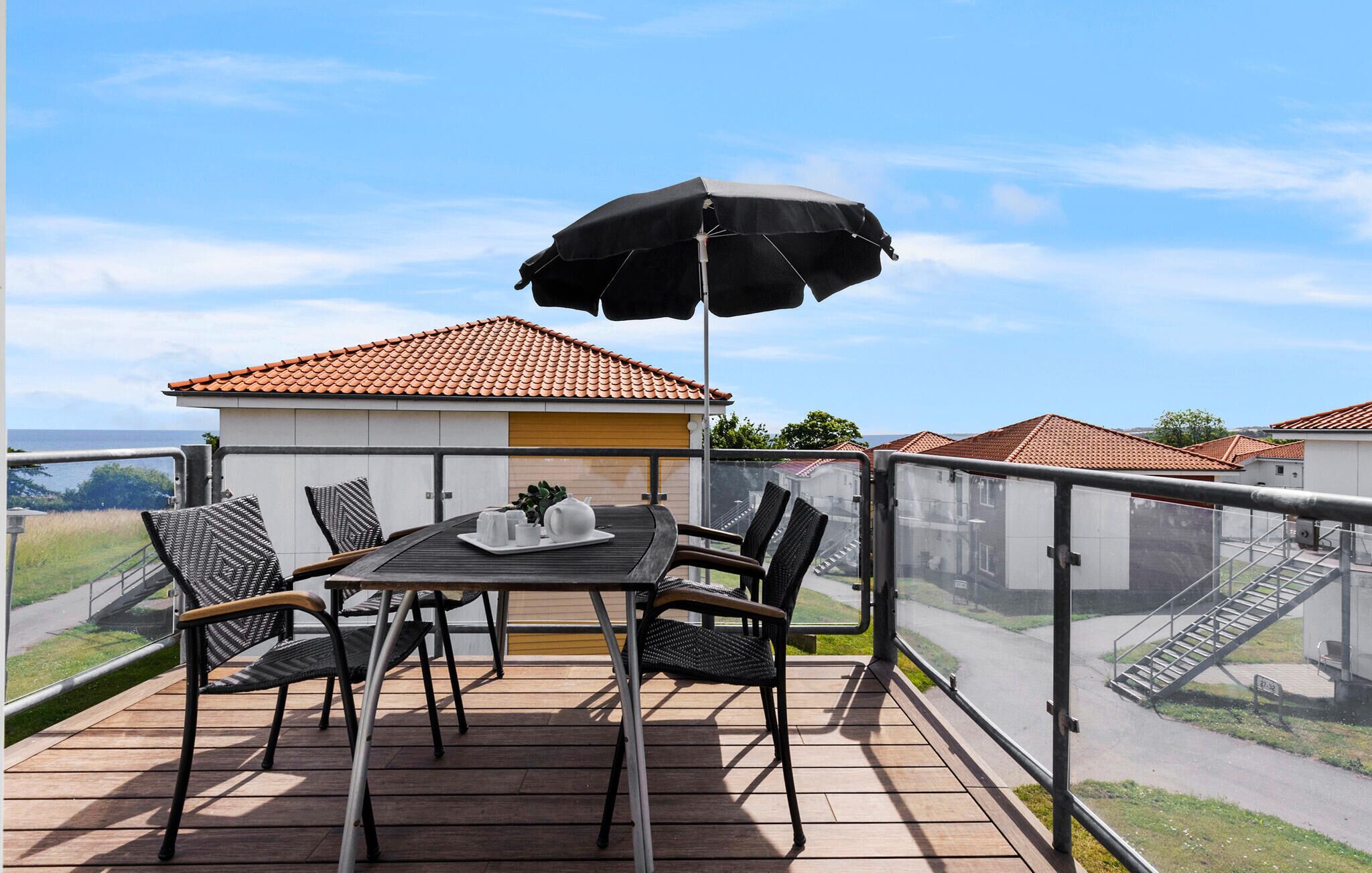 Een balkon met een tafel, stoelen en een zwarte parasol.