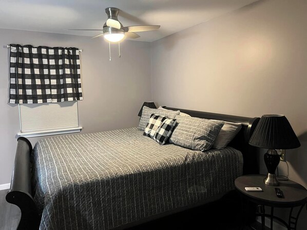 Een slaapkamer met een bed, een plafondventilator, een nachtkastje en een lamp.