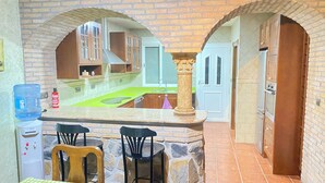 Una cocina con encimera verde, dos sillas negras, un dispensador de agua y una pared de piedra.