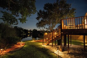 Eine Holzterrasse mit einer Treppe, die zu einem Gebäude führt, umgeben von Bäumen und einem Gewässer.