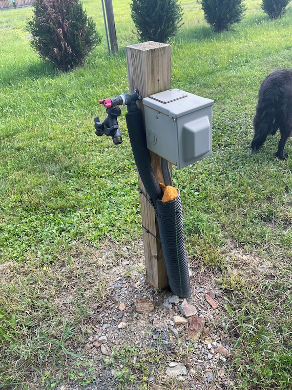 A wooden post with a black hose attached to it, connected to a grey electrical box.