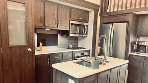 A modern kitchen with dark wood cabinets, stainless steel appliances, and a central island with a sink. - Grand Lodge Along Best Elk Viewing Road (Benezette)