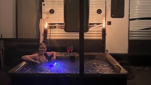 A person relaxing in a hot tub with a view of a trailer in the background. - Grand Lodge Along Best Elk Viewing Road (Benezette)