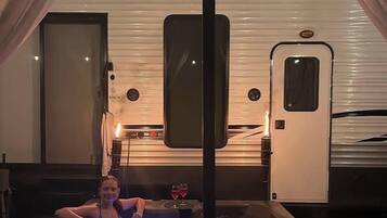 A person relaxing in a hot tub with a view of a trailer in the background.
