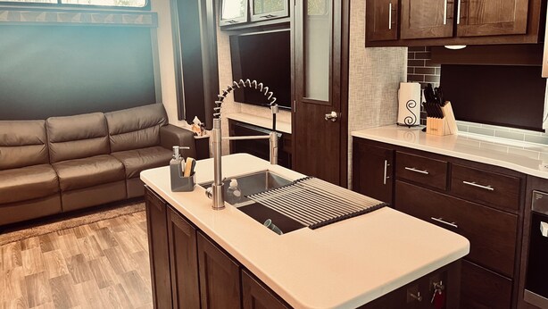A compact kitchen with a built-in stove, a sink, and a countertop. There is a brown leather sofa in the adjacent living area. - Grand Lodge Along Best Elk Viewing Road (Benezette)