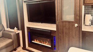A modern living room with a flat-screen TV mounted above a fireplace, wooden cabinets, and a leather sofa. - Grand Lodge Along Best Elk Viewing Road (Benezette)