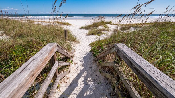 A wooden boardwalk leading to a beach with sand and grassy dunes. - Flamingo Beach Hideaway (St. Augustine)