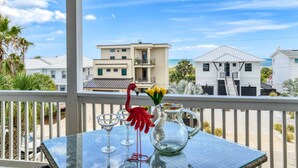 A balcony with a table set for two, overlooking a beach with houses and a clear sky. - Flamingo Beach Hideaway (St. Augustine)