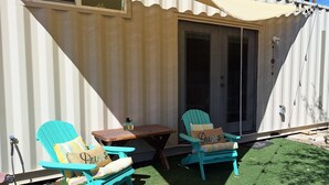 A covered outdoor seating area with two chairs and a table, a door, and a window.