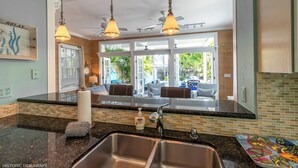 A kitchen with a double sink, two pendant lights, and a view to a patio area. - Boomerang Boathouse (Key West)