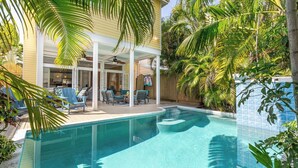 A swimming pool with a covered patio area, surrounded by lush greenery and a wooden fence. - Boomerang Boathouse (Key West)