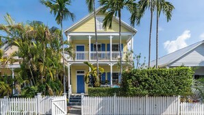 A two-story yellow house with a balcony, surrounded by palm trees and a white picket fence. - Boomerang Boathouse (Key West)