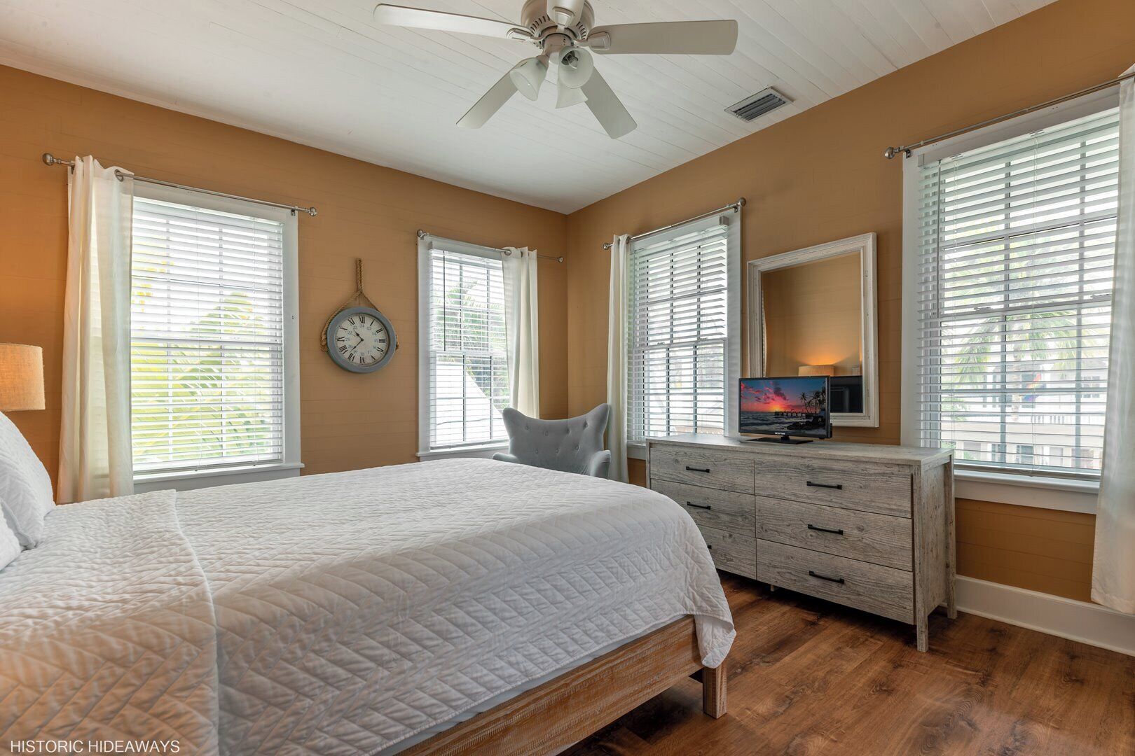 A bedroom with a large bed, a dresser, a television, and a ceiling fan.