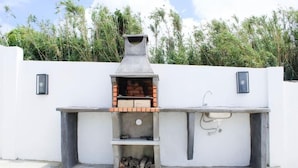 Een buitenkeuken van bakstenen met een schoorsteen, een spoelbak en een houtopbergruimte.