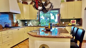 A kitchen with a central island, light-colored cabinets, and a view of greenery outside. - Charming 5-bed house with sweeping ocean views in delightful San Jose Del Cabo. (San Jose Del Cabo)