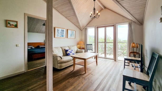 A cozy room with a wooden floor, a sofa, a table, and a balcony with outdoor furniture. - Cozy home in Tjörn with sauna (Tjörn)