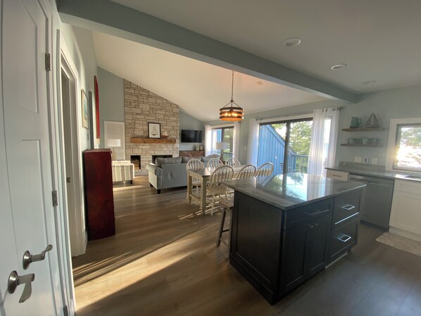 A spacious kitchen with a large island, a dining area with white chairs, a fireplace, and a stone accent wall.