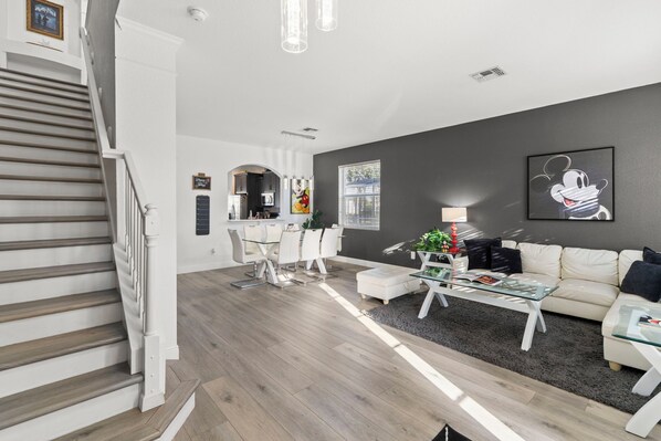 Un salon moderne avec un escalier, un coin repas et une cuisine en arrière-plan.