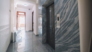 Un couloir avec un mur de marbre, un ascenseur et une poubelle.