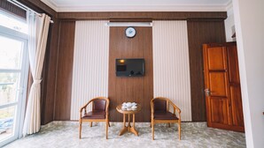 Une chambre d’hôtel avec un mur lambrissé en bois, un téléviseur à écran plat fixé au-dessus d’une petite table sur laquelle se trouve un service à thé, deux fauteuils en osier et une porte en bois.