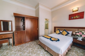 A hotel room with a bed, a wooden wardrobe, a desk with a mirror, and a wall-mounted light fixture. - Chau Gia Hotel Da Lat (Xuan Huong - Da Lat)
