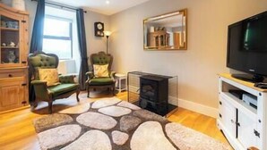 A living room with a fireplace, a television, and a stone-patterned rug. - Countryside Retreat Dingle (Municipal District of Castleisland-Corca Dhuibhne)