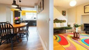 A modern interior with a dining area featuring a wooden table and chairs, a kitchen in the background, and a living room with a green sofa and a colorful rug. - Countryside Retreat Dingle (Municipal District of Castleisland-Corca Dhuibhne)