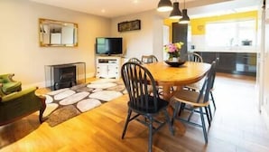 A modern kitchen with a dining area, wooden flooring, and a television on a cabinet. - Countryside Retreat Dingle (Municipal District of Castleisland-Corca Dhuibhne)
