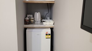 Een compacte kitchenette met een magnetron, een kleine koelkast en een plank met keukengerei.