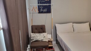 Hotelkamer met een bed, een stoel, een klein tafeltje, een ingebouwde airconditioner en een inspirerende poster.