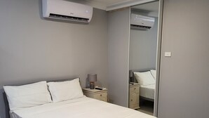 Een moderne slaapkamer met een bed, nachtkastje, lamp en een airconditioner.