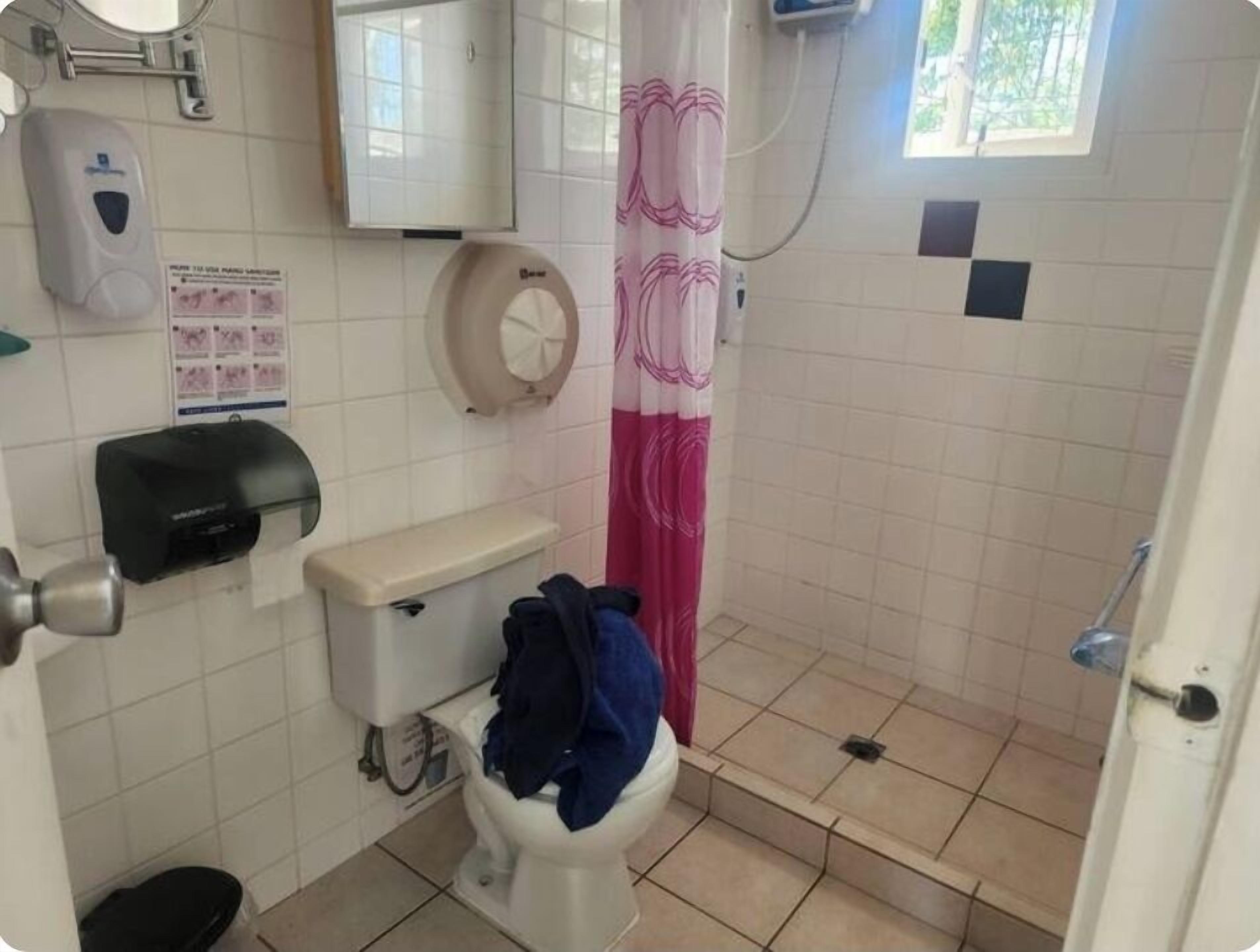 Un baño pequeño con inodoro, secamanos, dispensador de toallas de papel, cortina de ducha y ventana.