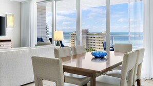Ein modernes Hotelzimmer mit großem Balkon, einer Essecke mit Holztisch und Stühlen sowie einem an der Wand montierten Fernseher.