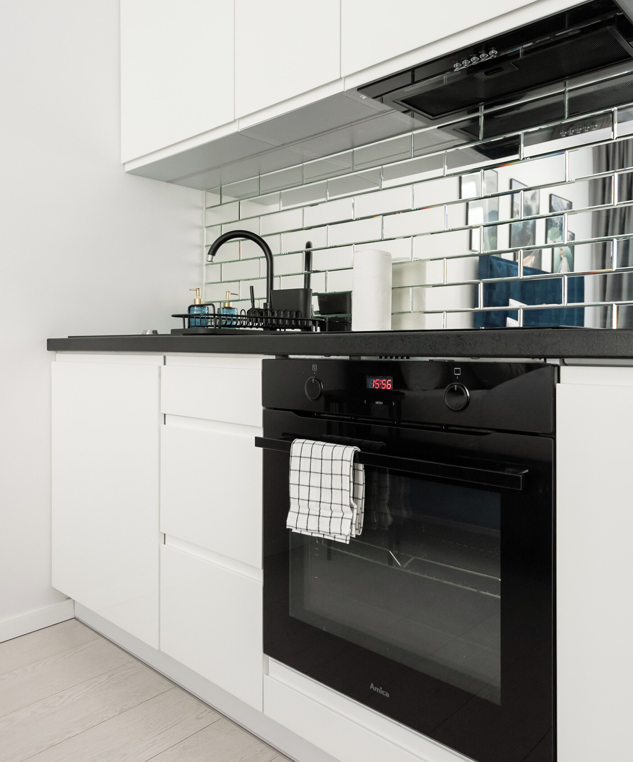 Una cocina moderna con armarios blancos, un horno negro y un reloj digital que marca las 15:56.