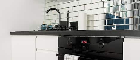 Una cocina moderna con armarios blancos, un horno negro y un reloj digital que marca las 15:56.