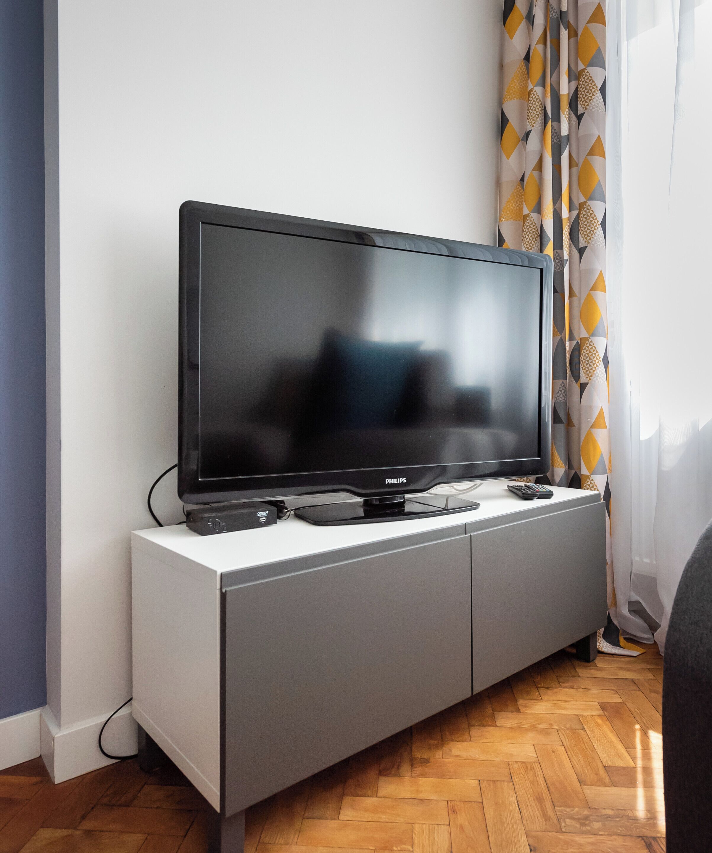 Un téléviseur à écran plat posé sur un meuble blanc, avec une télécommande dessus.