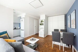 Ein modernes Wohnzimmer mit einer Couch, einem Esstisch mit Stühlen, einer Küchenzeile und einem Flur, der zum Schlafzimmer führt.