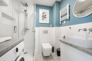 A modern bathroom with a glass-enclosed shower, a white toilet, a sink with a mirror, and a wall-mounted towel rack.